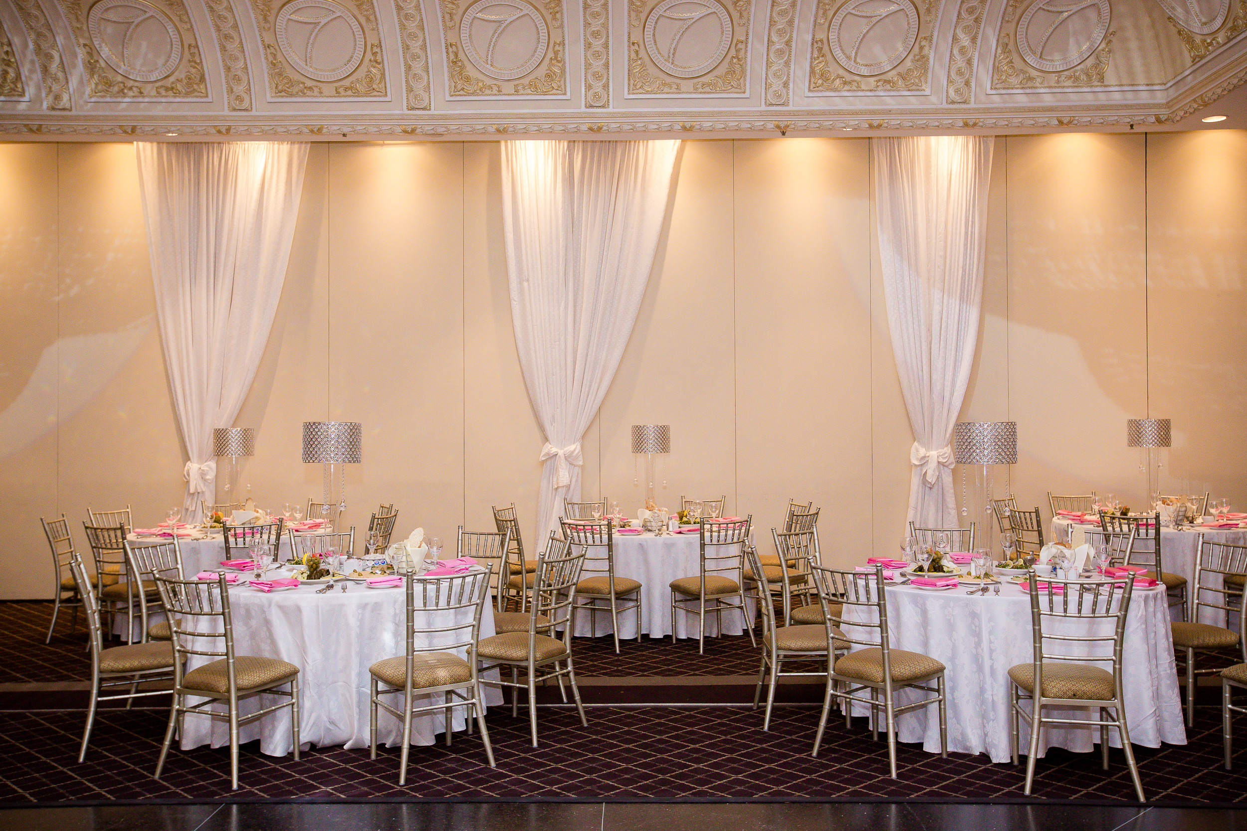 Elegant wedding reception hall with round tables, gold chairs, and soft drapery